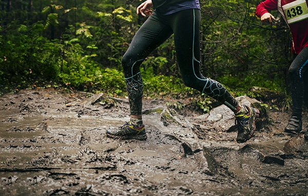 dirty feet woman runner run mountain trail in autumn through mud and puddles